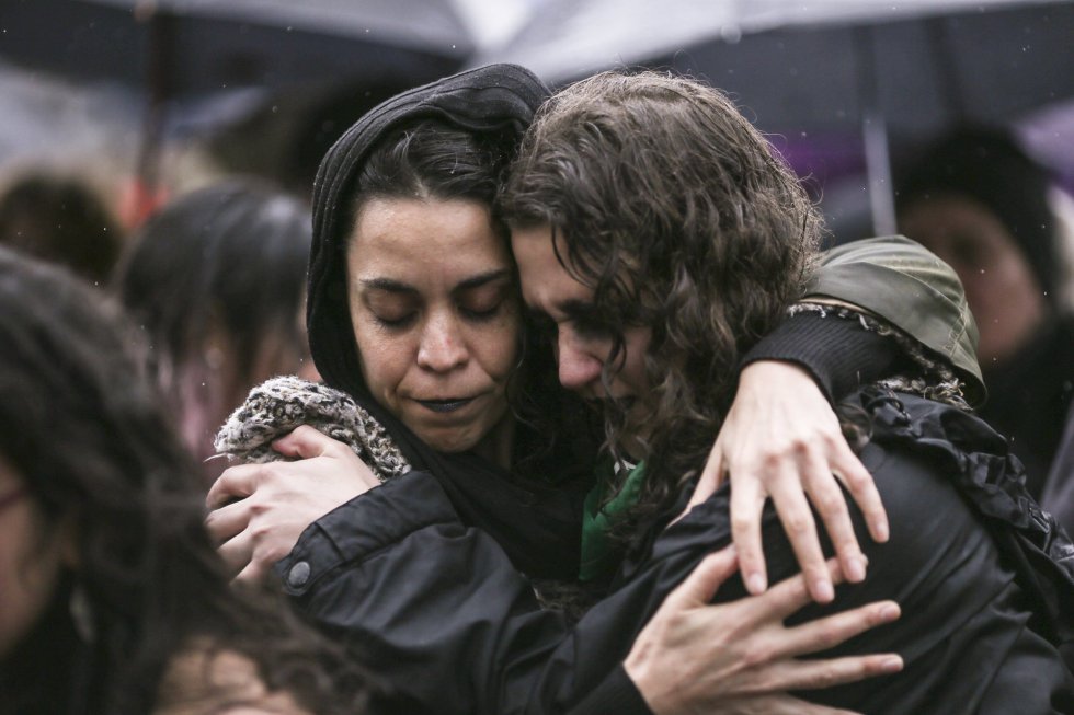 Dos mujeres jóvenes abrazandose bajo la lluvia, tristes.